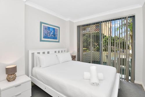 a white bedroom with a white bed and a window at Ocean Palms Unit 1 in The Entrance