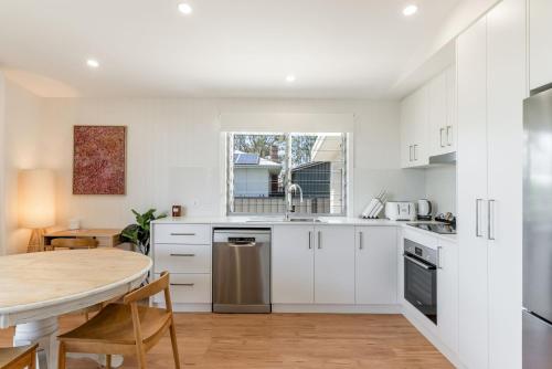 a kitchen with white cabinets and a wooden table at Park Lane - 4B Wattle Street in Evans Head