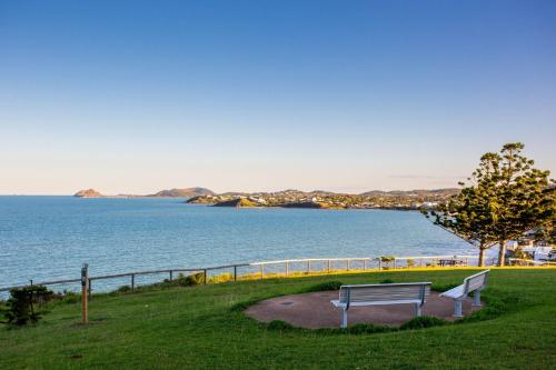 a bench sitting on the grass near the water at Ocean View Apartment Yeppoon in Yeppoon
