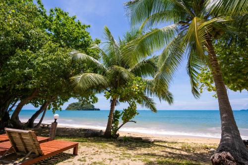 a beach with a bench and palm trees and the ocean at Libong Beach Resort in Ko Libong