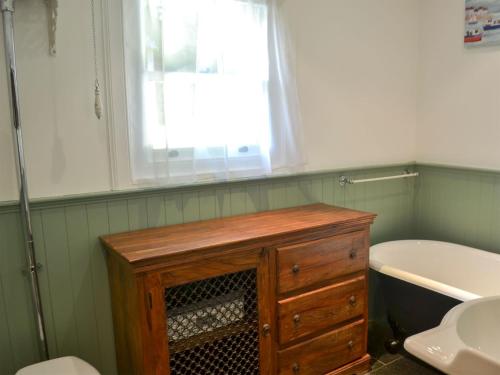 a bathroom with a wooden dresser and a bath tub at Sluice Keepers Cottage in Skelbo