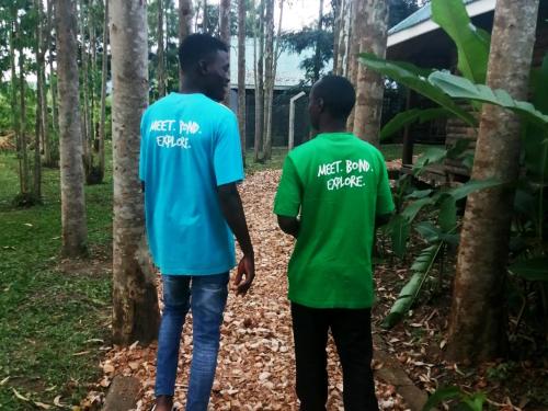 two men wearing green and blue shirts standing in the woods at Murchison Backpackers in Masindi