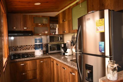 a kitchen with wooden cabinets and a stainless steel refrigerator at Acogedora Cabaña En Tabio con zonas verdes y BBQ in Tabio