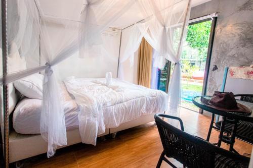 1 dormitorio con 1 cama con cortinas blancas y mesa en บ้านสวีทคาบาน่า และบ้านสวีทโอโซนBy The mountain Ozone บ้านโอโซนขุนเขาแก่งกกระจาน en Ban Song Phi Nong