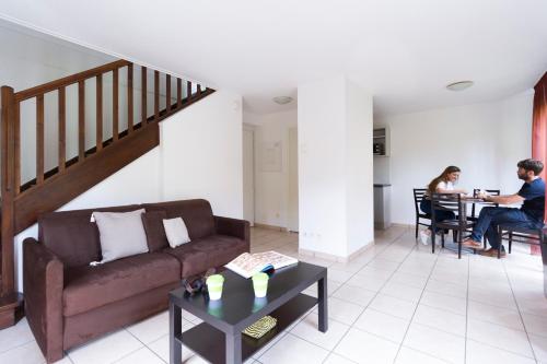 a living room with a couch and two people sitting at a table at Garden & City Lyon - Marcy in Marcy-lʼÉtoile