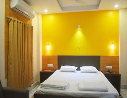 a bedroom with a large bed with a yellow wall at Hotel Glory Grand, Rajgir in Rājgīr