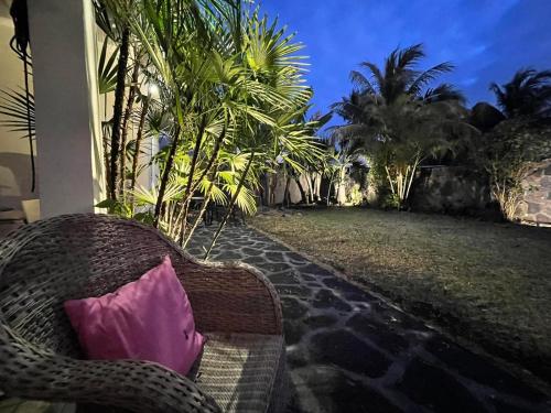 a wicker chair with a pink pillow on a patio at Villamarday - Coquette villa privée au bord de l'océan in Pointe aux Cannoniers