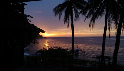 a sunset over the ocean with palm trees at Aquaventure Reef Club in Mabini