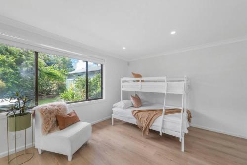 a white bedroom with a bunk bed and a chair at Two Dreamy Properties In One in Culburra Beach