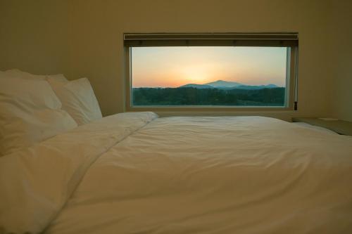 a large white bed in a room with a window at Chuidasun Resort Tea & Meditation in Seogwipo