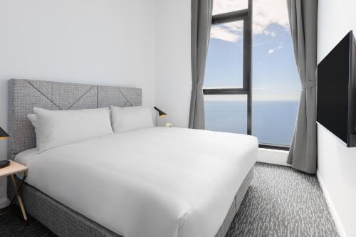 a white bed in a room with a window at Meriton Suites Surfers Paradise in Gold Coast