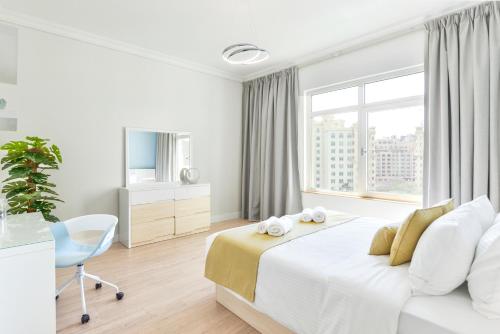 een witte slaapkamer met een bed, een bureau en een raam bij Shoreline · Beachfront Luxury Palm Jumeirah · Free 5* Beach Resorts Access in Dubai