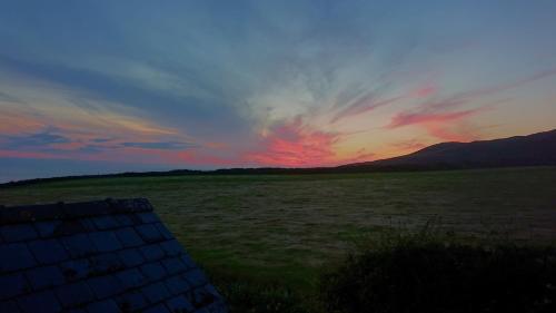 a sunset in a field with a large field at The Lobster Pot Cottage Church Bay in Llanrhyddlad