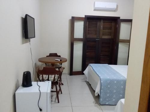a small room with a bed and a table and a television at Residencial Seestern - Suítes in Cananéia