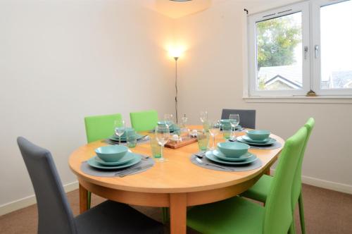 a dining room with a wooden table and green chairs at Pedals and Paddles in Innellan