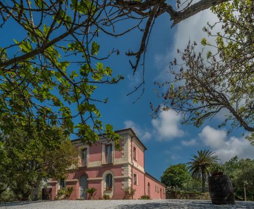 un vieux bâtiment rose avec des arbres au premier plan dans l'établissement Agriturismo Piano del Monaco, à Marcellinara