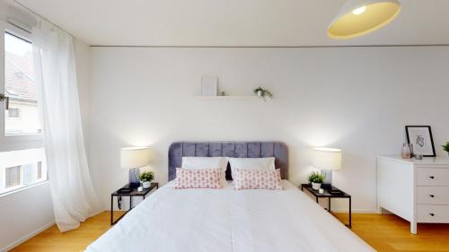 a white bedroom with a large bed with two pillows at Sublime contemporary apartment in the city centre in La Chaux-de-Fonds
