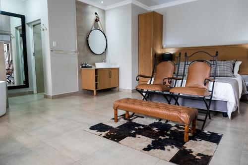 a bedroom with a bed with two chairs and a mirror at Villa Gracia Guesthouse in Klerksdorp