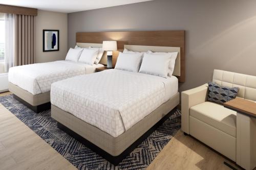 a hotel room with two beds and a chair at Candlewood Suites - Detroit - Auburn Hills by IHG in Auburn Hills