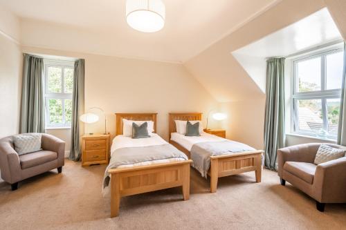 two beds in a room with two chairs and windows at Corriness House in Poolewe