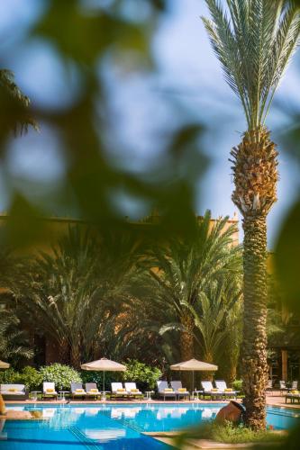a pool with a palm tree and chairs and umbrellas at Berbère Palace in Ouarzazate