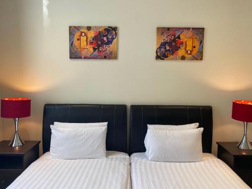 two beds in a room with two lamps and paintings at Grand Plaza Serviced Apartments in London