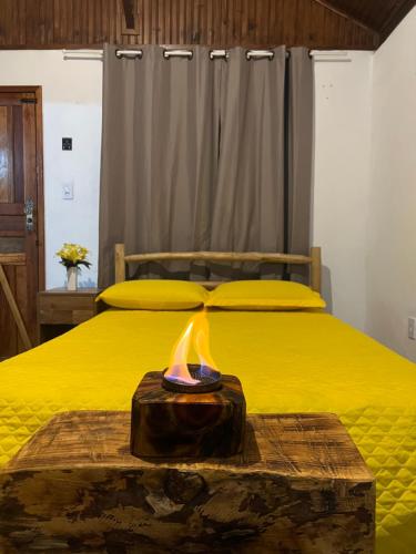 Una cama amarilla con un bloque de madera con fuego. en Chales Mirante Pedra Selada, en Visconde De Maua