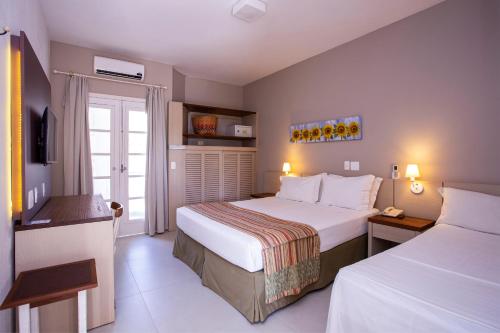 a hotel room with two beds and a television at Ciribaí Praia Hotel in Pauba