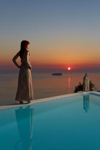 a woman standing on the edge of a swimming pool at sunset at Athermi Suites - Adults Only in Megalokhori