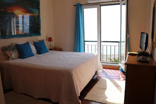 a bedroom with a bed with blue pillows and a balcony at Casa do Sol in Ponta do Sol