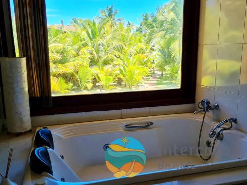 a tub in a bathroom with a window and palm trees at Villa Bora Bora - Frente mar, Praia do Forte in Praia do Forte