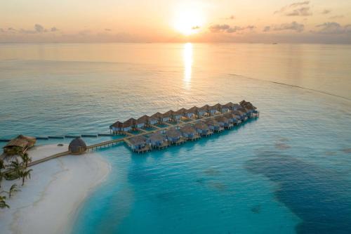 ダンゲシにあるOutrigger Maldives Maafushivaru Resortの夕日の海のリゾートの空中ビュー