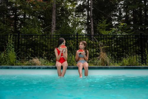 two young girls sitting on the edge of a swimming pool at Chalet Blue Jay Spa at Fiddler's Lake in Mille-Isles
