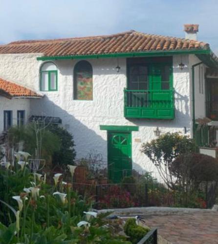 ein weißes Haus mit grünen Türen und einem Balkon in der Unterkunft Hostal La Cestería Pueblito Boyacense in Duitama