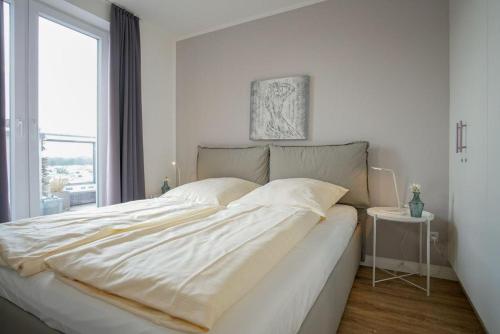 1 cama blanca grande en un dormitorio blanco con ventana en Strandpark-Grossenbrode-Haus-Seestern-Wohnung-38-Strandoase-im-Strandpark, en Großenbrode