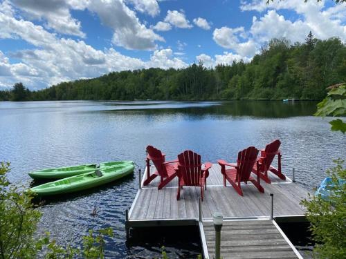 a dock with chairs and a boat on a lake at Chalet Kabana Spa au bord du lac in Sainte-Émélie-de-lʼÉnergie