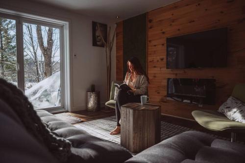 a woman sitting in a living room reading a book at Chalet Kabana Spa au bord du lac in Sainte-Émélie-de-lʼÉnergie
