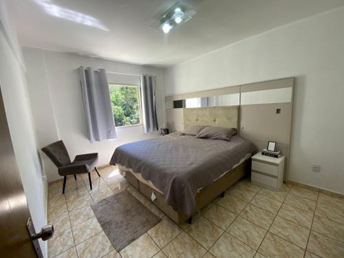 a bedroom with a bed and a chair and a window at Apartamento VIP Centro Serra Negra - Familiar in Serra Negra