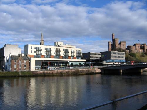 a large white building next to a river with a bridge at Highland Apartments by Mansley in Inverness