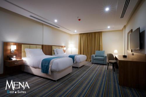 a hotel room with two beds and a desk and a tv at Mena East Suites Dammam in Dammam