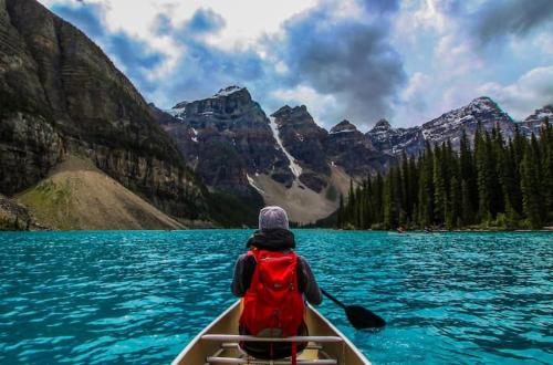 a person in a canoe on a lake with mountains at Incredible Mountain View Townhouse in DT Canmore w/ A/C & U/A Parking in Canmore