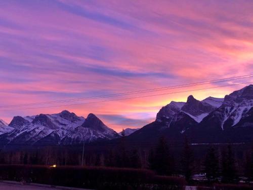 a sunset over a mountain range with snowy mountains at Incredible Mountain View Townhouse in DT Canmore w/ A/C & U/A Parking in Canmore