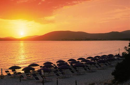 a group of chairs and umbrellas on a beach at sunset at Hotel Angedras in Alghero