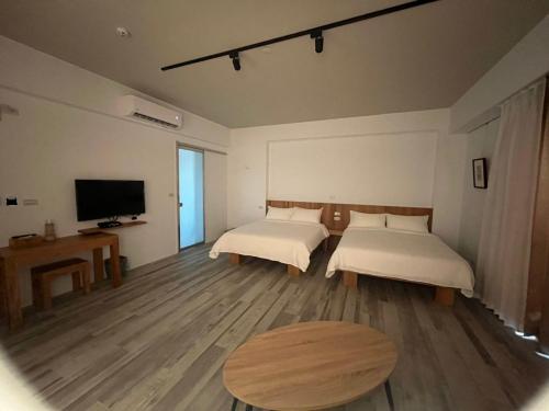 HuxiにあるWutong Homestayのベッド2台、テーブル、テレビが備わる客室です。
