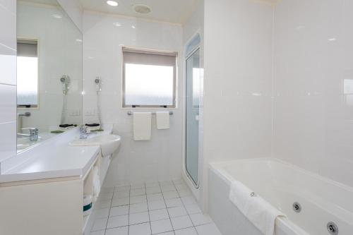 a white bathroom with a tub and a sink at Village Motel in Havelock North