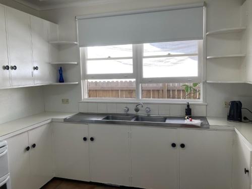 a white kitchen with a sink and a window at Beach House On Golf in Mollymook