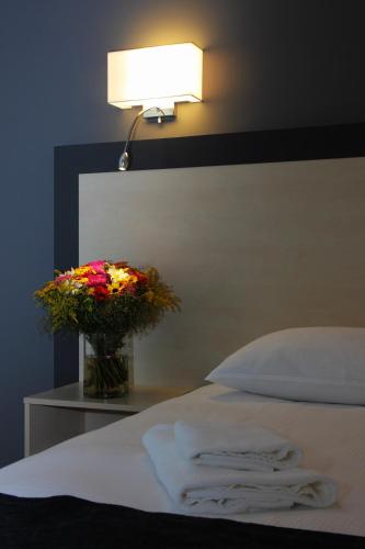 a bed with a vase of flowers and a lamp at Aurora Hotel Klaipeda in Klaipėda