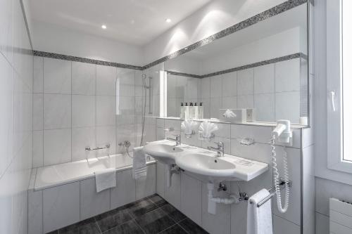 a white bathroom with a sink and a tub at Blatter's Arosa Hotel & Bella Vista SPA in Arosa