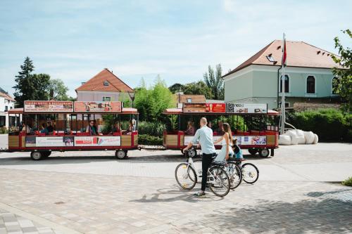 a man and a woman riding a bike in front of a trolley at Atmoszféra Apartman in Sárvár