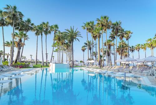 a swimming pool with palm trees and lounge chairs at Leonardo Plaza Cypria Maris Beach Hotel & Spa in Paphos City